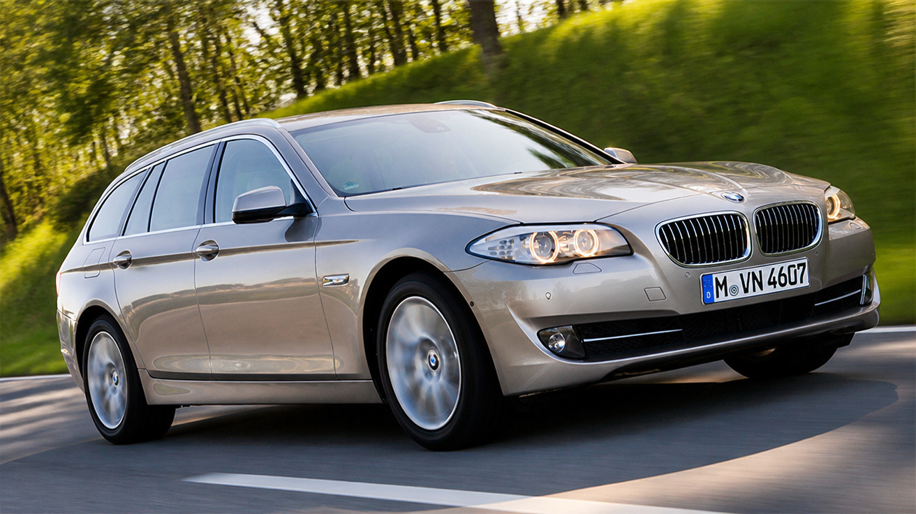 Automóvel BMW cinzento a circular numa estrada rodeada por árvores verdes.