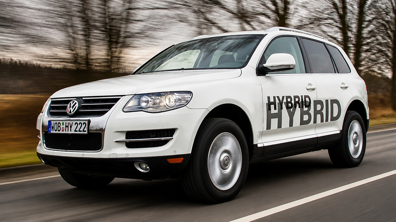 Carro SUV branco Volkswagen híbrido em estrada com árvores desfocadas ao fundo.