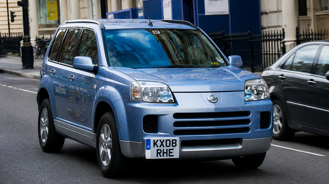 Carro azul Nissan SUV a circular numa estrada urbana com matrícula britânica.