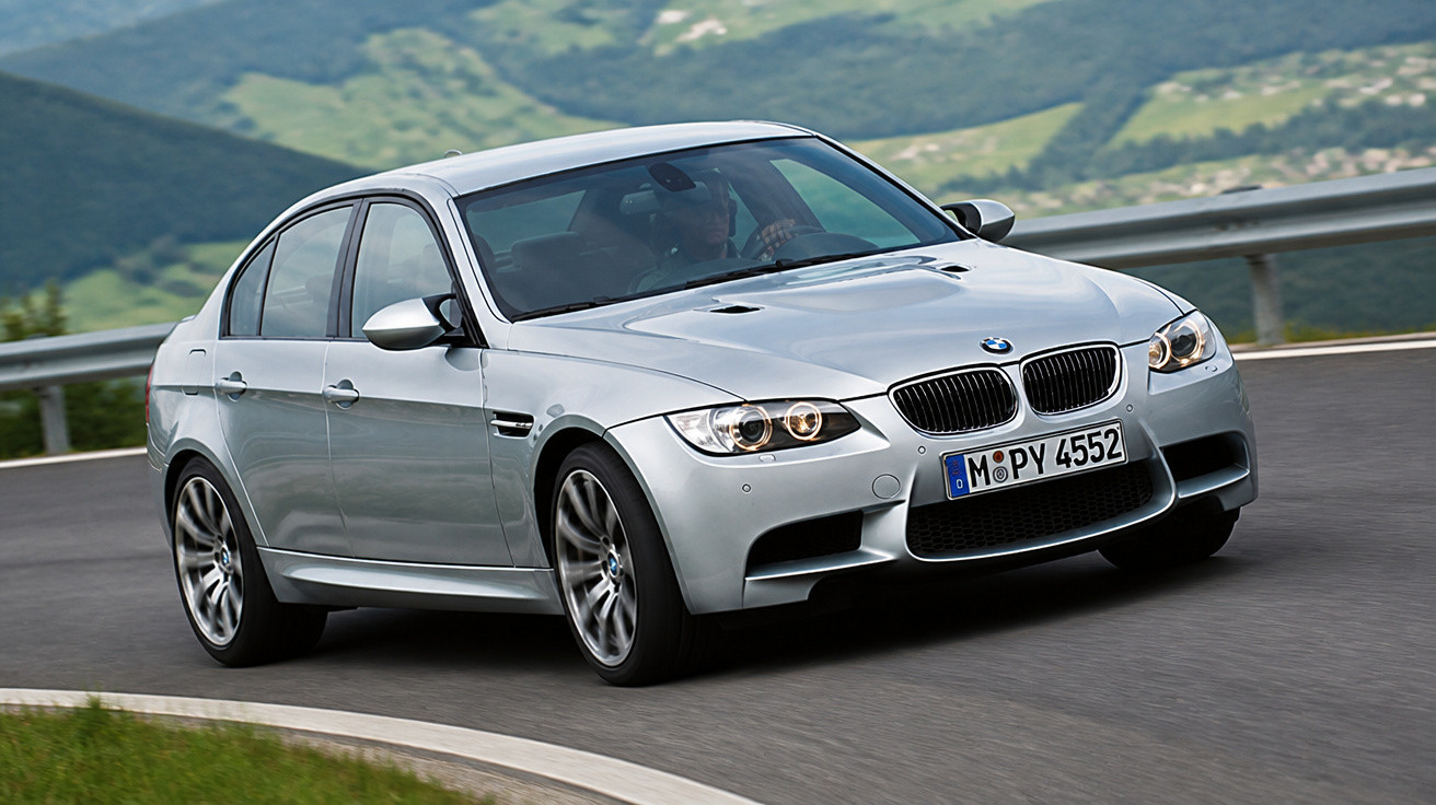 Carro BMW prata a curvar numa estrada de montanha com relva e guarda-rail ao lado.