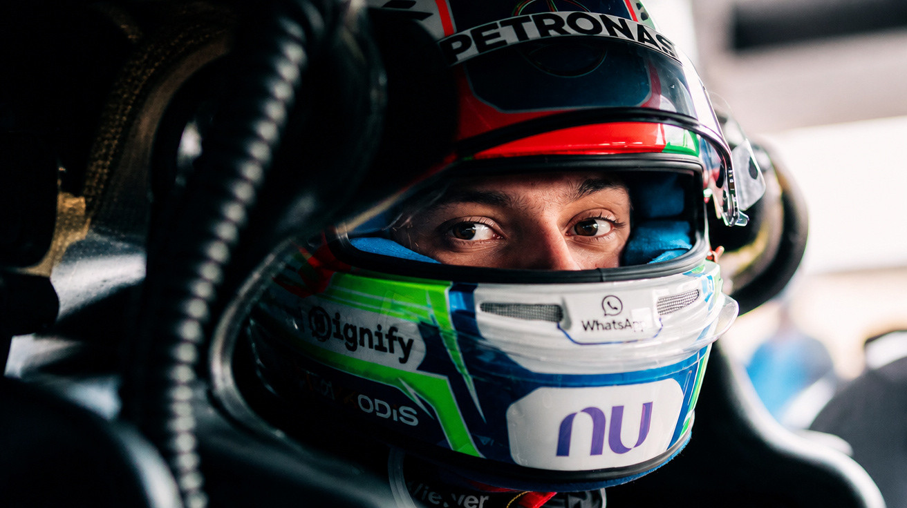 Piloto de corrida com capacete colorido sentado no cockpit de um carro de Fórmula 1.